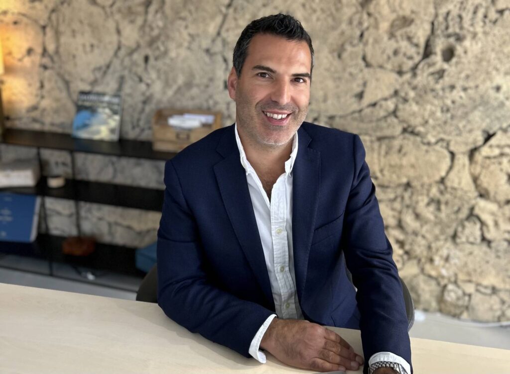 Portrait professionnel d'un homme d'affaires au bureau Homme souriant en veste bleu marine assis à son bureau devant un mur en pierre.